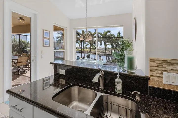 Kitchen with dark stone counters, sink, a water view, white cabinetry, and lofted ceiling