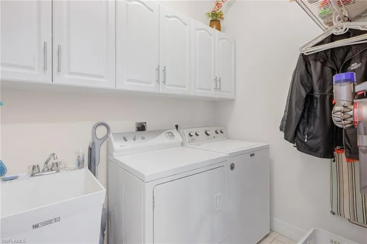 Clothes washing area with washer and dryer, cabinets, light tile patterned floors, and sink