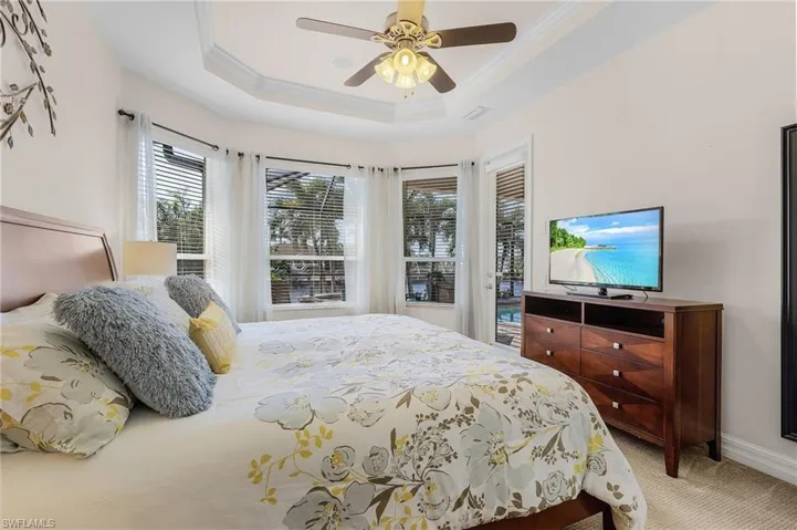 Carpeted bedroom featuring access to exterior, a tray ceiling, ceiling fan, and crown molding