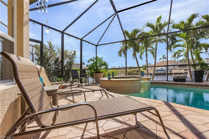 View of swimming pool featuring an in ground hot tub, a patio, a water view, and glass enclosure