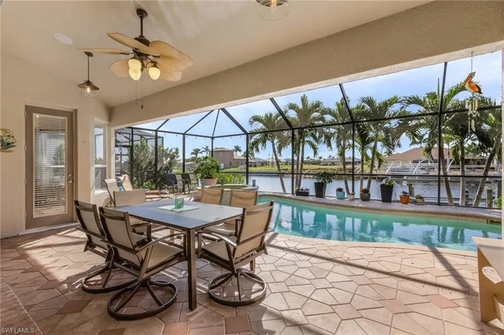 View of pool featuring a patio area, ceiling fan, a water view, and glass enclosure