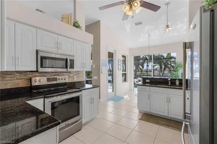 Kitchen featuring pendant lighting, lofted ceiling, dark stone counters, white cabinetry, and stainless steel appliances
