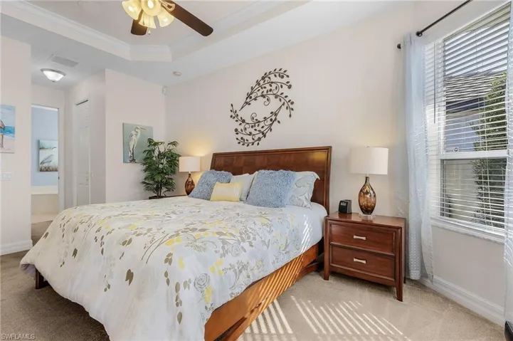 Bedroom with ceiling fan, a raised ceiling, crown molding, light carpet, and a closet