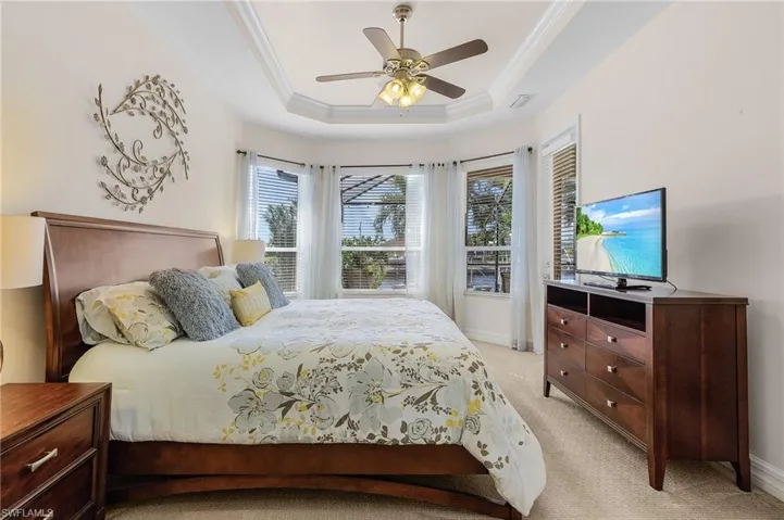 Carpeted bedroom featuring a tray ceiling, ceiling fan, and crown molding
