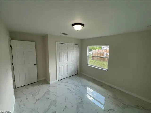 Unfurnished bedroom with marble finish flooring, baseboards, and a closet