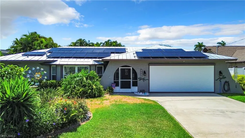 View of front of home featuring a standing seam roof, solar panels, a front lawn, concrete driveway, and an attached garage