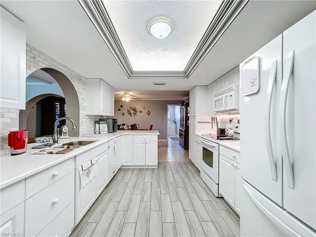 Kitchen featuring white appliances, light countertops, white cabinets, a sink, and backsplash