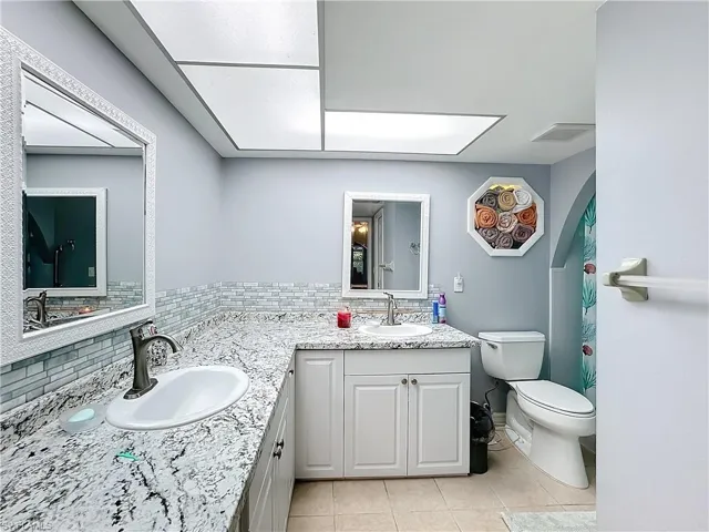 Full bath featuring vanity, toilet, tile patterned flooring, and tasteful backsplash