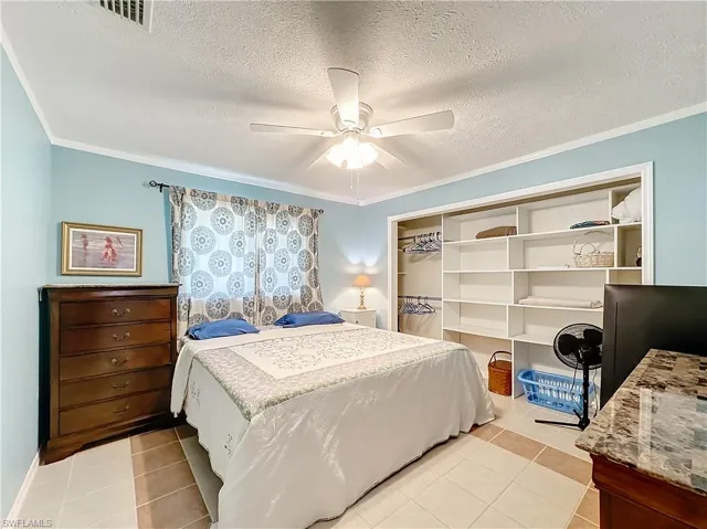 Bedroom featuring ceiling fan, visible vents, light tile patterned floors, a closet, and ornamental molding