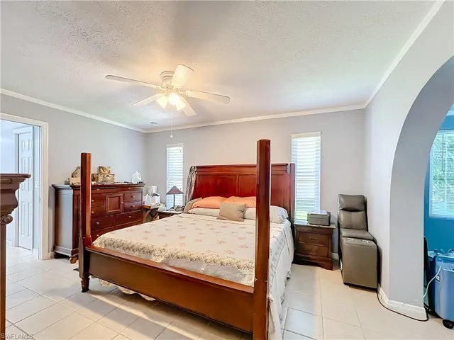 Bedroom featuring arched walkways, ceiling fan, baseboards, and light tile patterned flooring