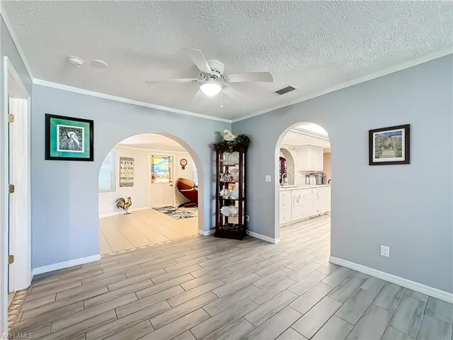 Corridor featuring arched walkways, light wood finished floors, and a textured ceiling