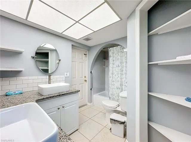 Full bathroom with visible vents, tile patterned flooring, shower / bath combination with curtain, toilet, and backsplash
