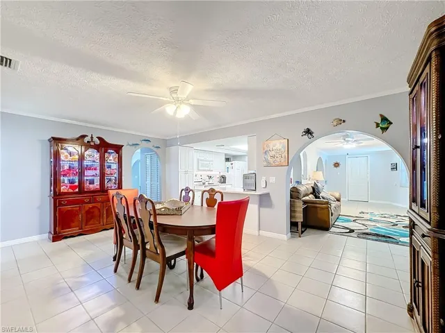 Dining space featuring arched walkways, a textured ceiling, a ceiling fan, light tile patterned floors, and ornamental molding