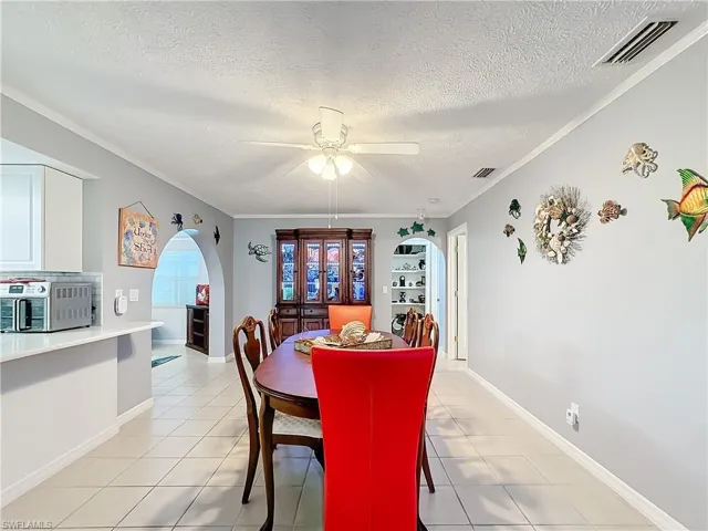 Dining space with light tile patterned floors, arched walkways, ceiling fan, and visible vents