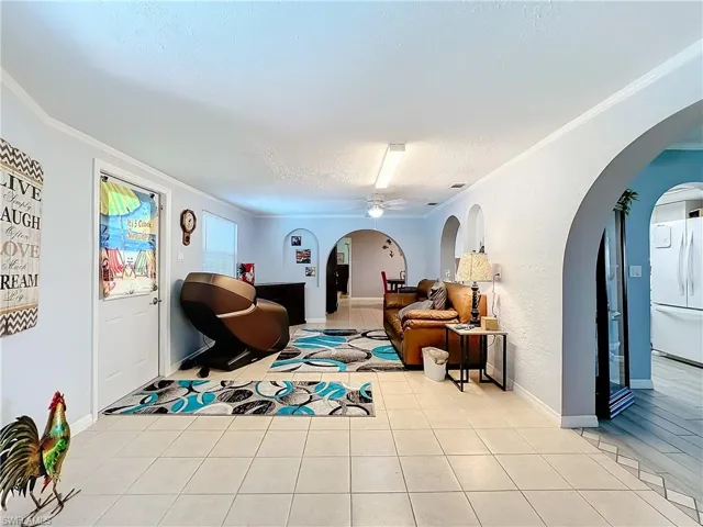 Living room featuring light tile patterned flooring, arched walkways, a textured ceiling, a ceiling fan, and ornamental molding