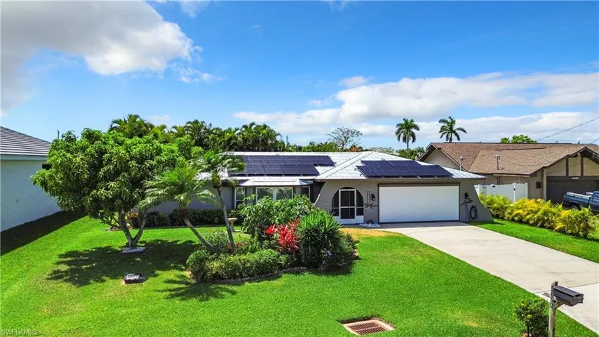 Ranch-style house with an attached garage, driveway, roof mounted solar panels, and a front lawn