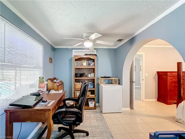 Office area featuring ceiling fan, a textured ceiling, crown molding, arched walkways, and light tile patterned flooring