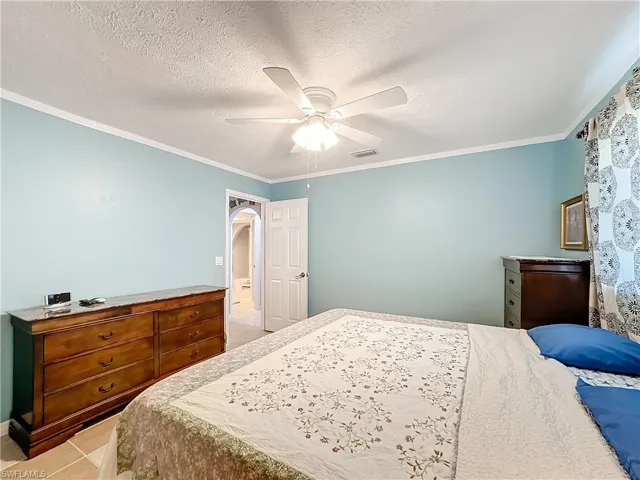 Bedroom featuring ceiling fan, visible vents, crown molding, arched walkways, and light tile patterned floors