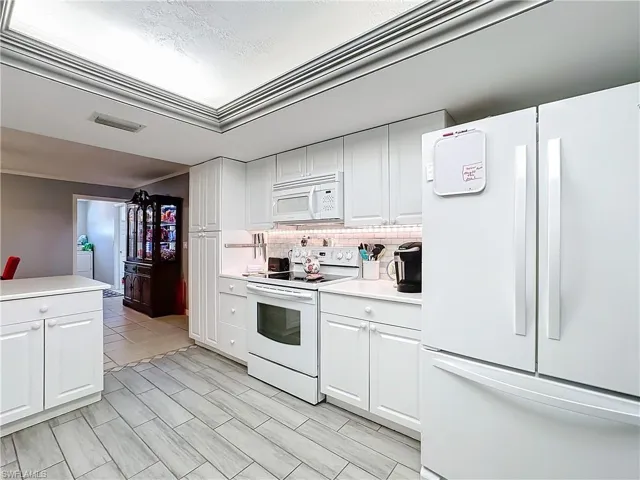 Kitchen featuring light countertops, decorative backsplash, white appliances, and white cabinetry
