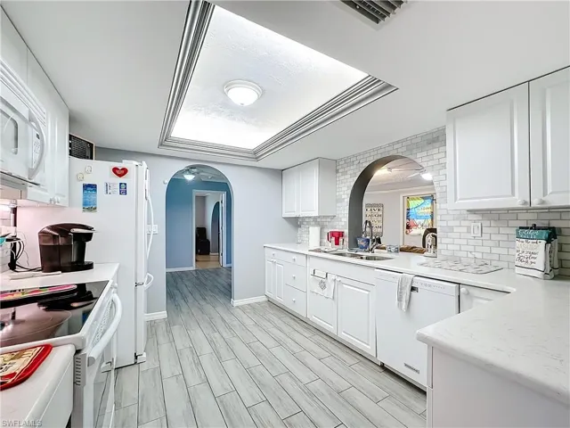 Kitchen with white appliances, arched walkways, a sink, and tasteful backsplash