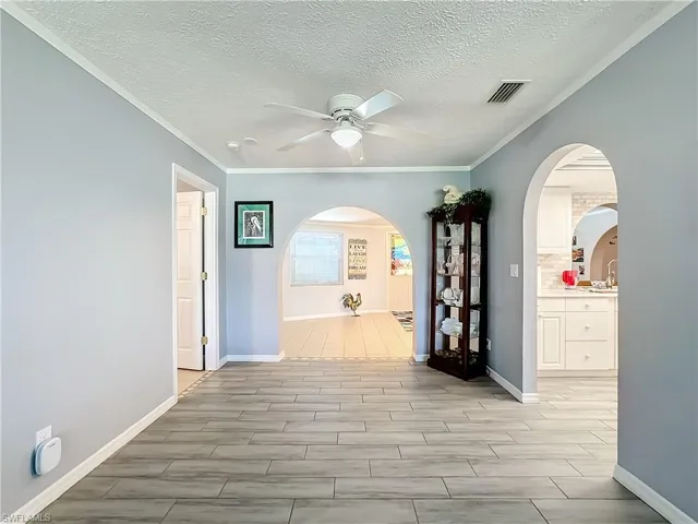 Hallway with visible vents, arched walkways, a textured ceiling, and ornamental molding