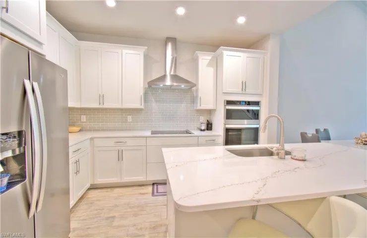 Kitchen with stainless steel appliances, a kitchen breakfast bar, white cabinets, and recessed lighting