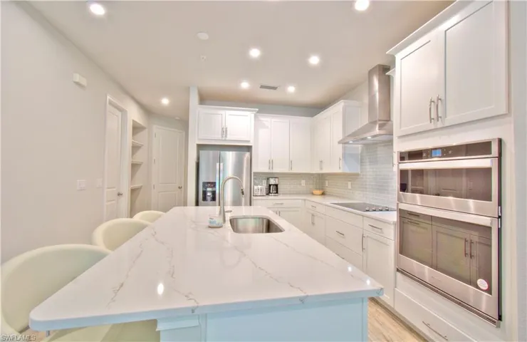 Kitchen featuring stainless steel appliances, white cabinets, a breakfast bar, light stone countertops, and a kitchen island with sink
