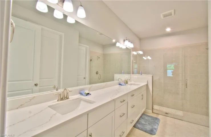 Bathroom featuring a stall shower, double vanity, a chandelier, and light tile patterned flooring