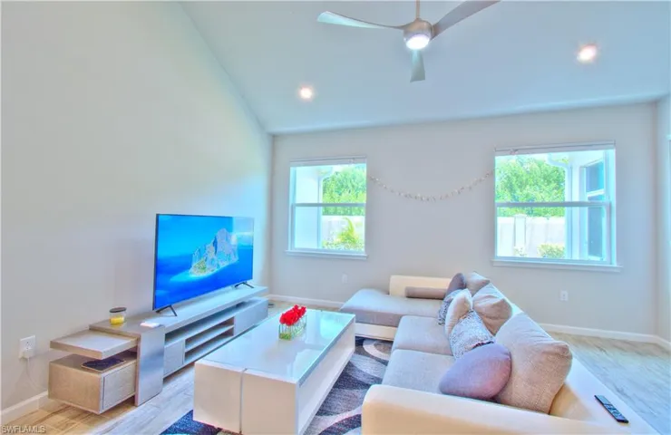 Living area with light wood-style flooring, ceiling fan, and lofted ceiling