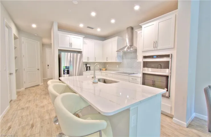 Kitchen with white cabinetry, a kitchen breakfast bar, an island with sink, stainless steel appliances, and light stone countertops