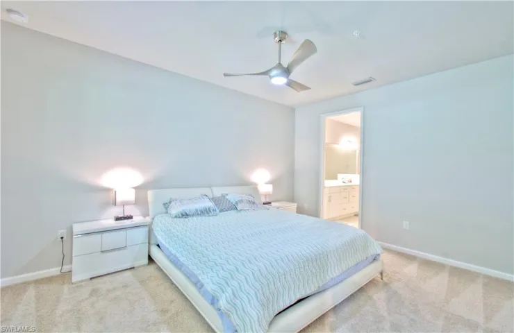 Bedroom with ceiling fan, light colored carpet, and connected bathroom