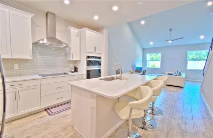 Kitchen featuring wood tiled floors, white cabinets, open floor plan, light stone counters, and recessed lighting