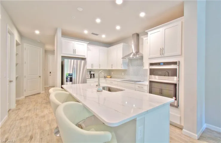 Kitchen featuring white cabinets, a breakfast bar area, an island with sink, light stone countertops, and stainless steel appliances