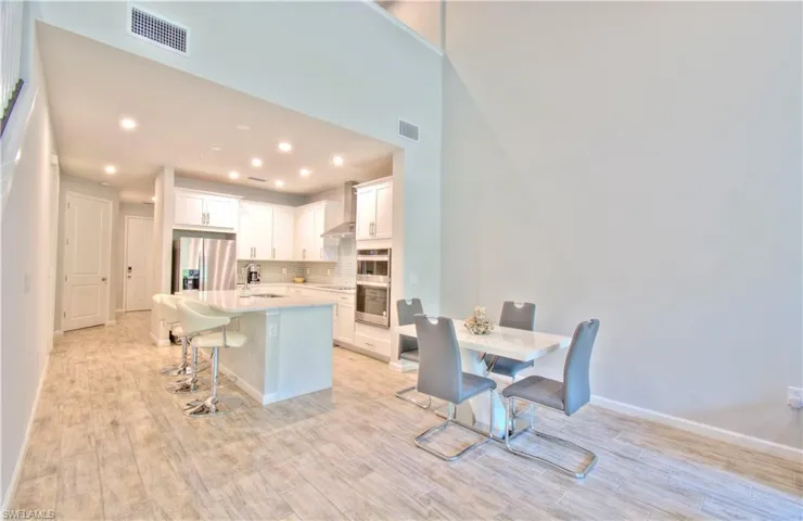 Kitchen featuring a breakfast bar, white cabinets, a center island with sink, light wood-style floors, and recessed lighting