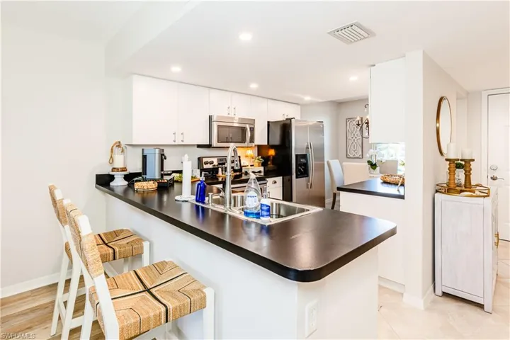Kitchen featuring appliances with stainless steel finishes, a kitchen bar, kitchen peninsula, sink, and white cabinetry