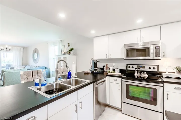 Kitchen with light tile patterned floors, appliances with stainless steel finishes, white cabinetry, a notable chandelier, and sink