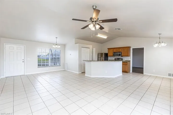 Kitchen with a chandelier, open floor plan, pendant lighting, brown cabinetry, and an island with sink