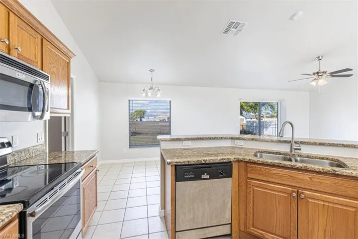 Kitchen with stainless steel appliances, brown cabinets, light tile patterned floors, light stone countertops, and plenty of natural light