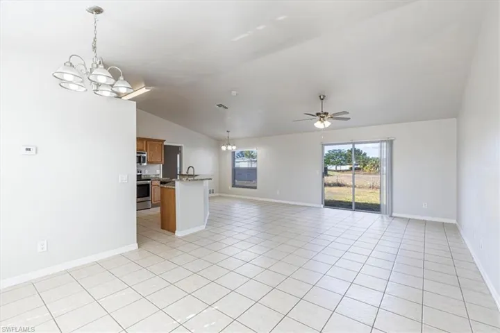 Unfurnished living room with a chandelier, lofted ceiling, a ceiling fan, and light tile patterned floors