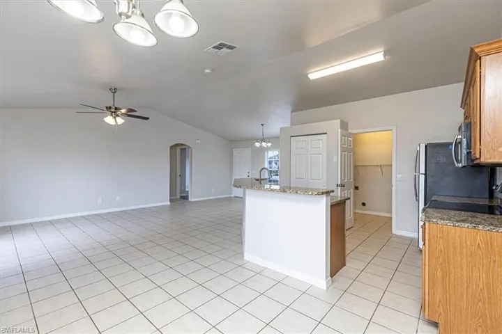 Kitchen with a chandelier, pendant lighting, arched walkways, light stone countertops, and a center island with sink