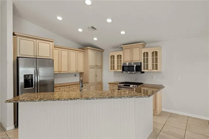 Kitchen featuring stainless steel appliances, visible vents, a center island with sink, and light tile patterned floors