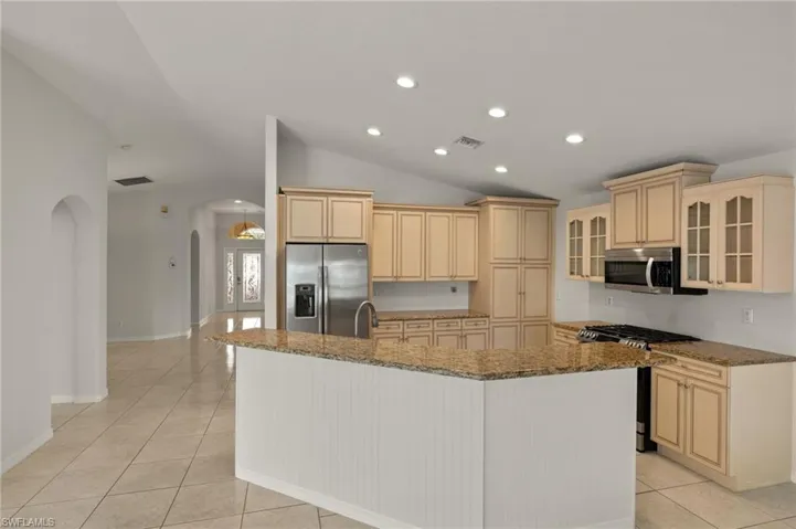 Kitchen featuring visible vents, arched walkways, appliances with stainless steel finishes, a kitchen island with sink, and vaulted ceiling