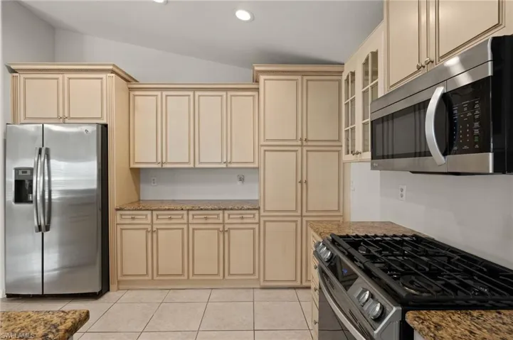 Kitchen with stainless steel appliances, cream cabinetry, light tile patterned floors, and light stone countertops