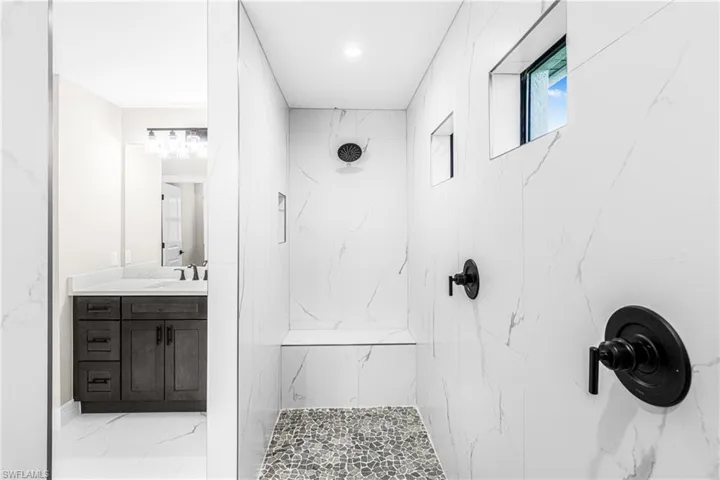 Bathroom featuring a marble finish shower, light marble finish flooring, and vanity