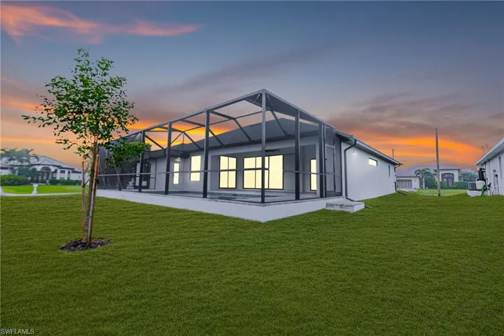 Back of property at dusk with a sunroom, a lanai, and a yard