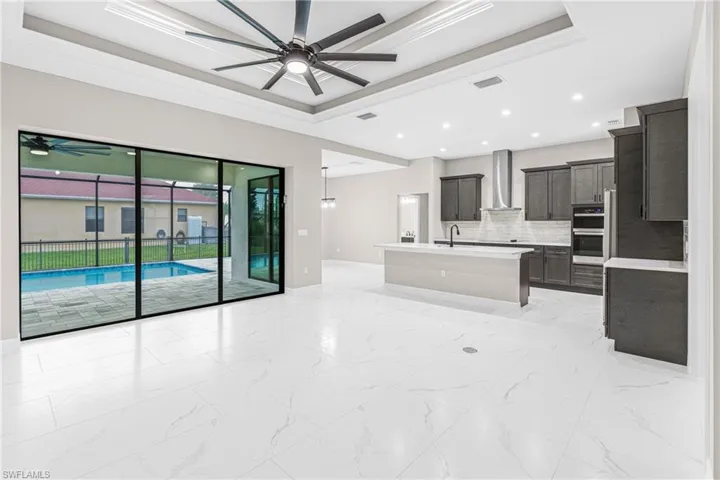 Kitchen featuring a raised ceiling, open floor plan, light marble finish floors, decorative backsplash, and a kitchen island with sink