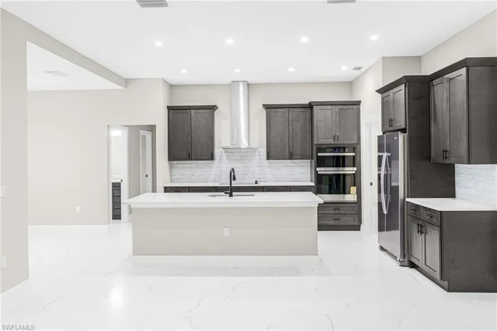 Kitchen with light marble finish floors, a kitchen island with sink, appliances with stainless steel finishes, light stone counters, and recessed lighting