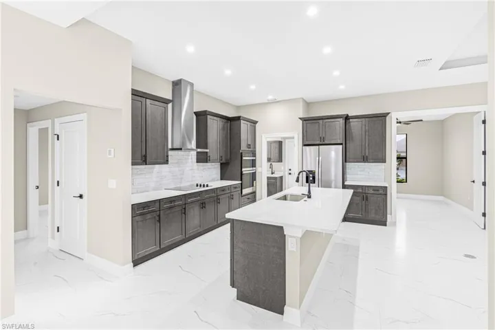 Kitchen featuring backsplash, appliances with stainless steel finishes, an island with sink, light stone countertops, and recessed lighting