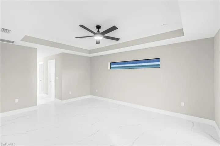 Empty room featuring a raised ceiling, ornamental molding, light marble finish flooring, and ceiling fan