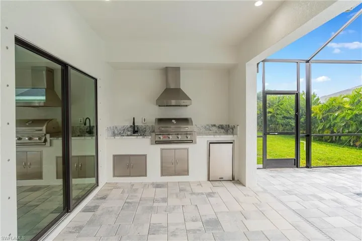 Kitchen with wall chimney exhaust hood, light stone counters, refrigerator, recessed lighting, and a sunroom
